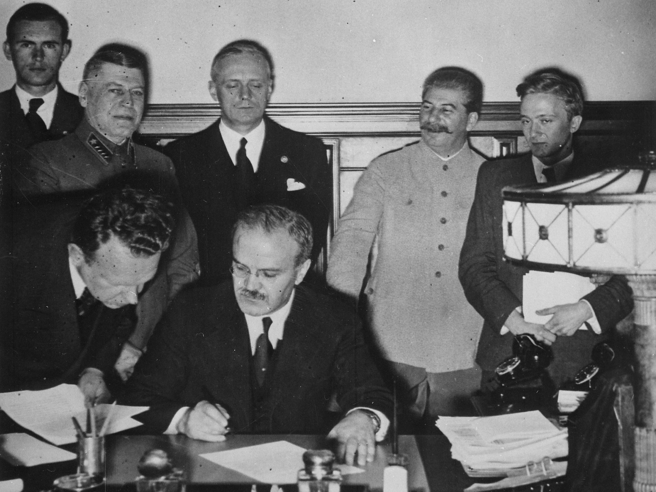 Molotov podepisuje 23. srpna 1939 pakt o neútočení mezi Německem a Sovětským svazem, vzadu stojí Joachim von Ribbentrop a Josif Stalin