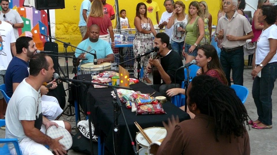 Lidé se pomalu scházejí a na stole mezi muzikanty se hromadí darované jídlo pro zdejší školku