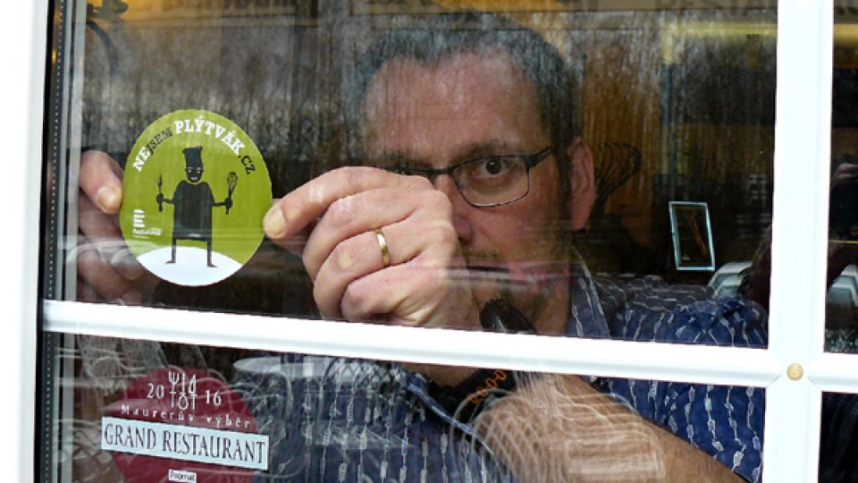 Redaktor Tomáš Mařas lepí samolepku Nejsem plýtvák na dveře restaurace