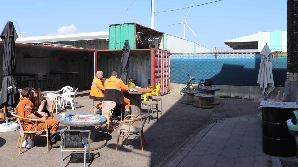 Část zaměstnanců přístavu sedí venku na zahrádce u stolečků vytvořených z prázdných špulek od kabelů