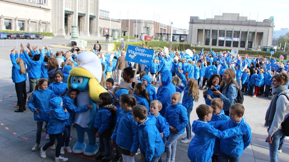 Děti v modrých tričkách se připravují na to, že vytvoří na počet šmoulího jubilea velké číslo šedesát 