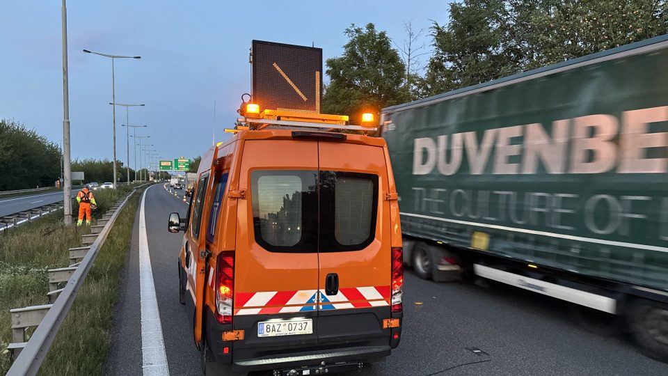 Malé oranžové auto s výstražnými světly u svodidla značí, že se tady pracuje