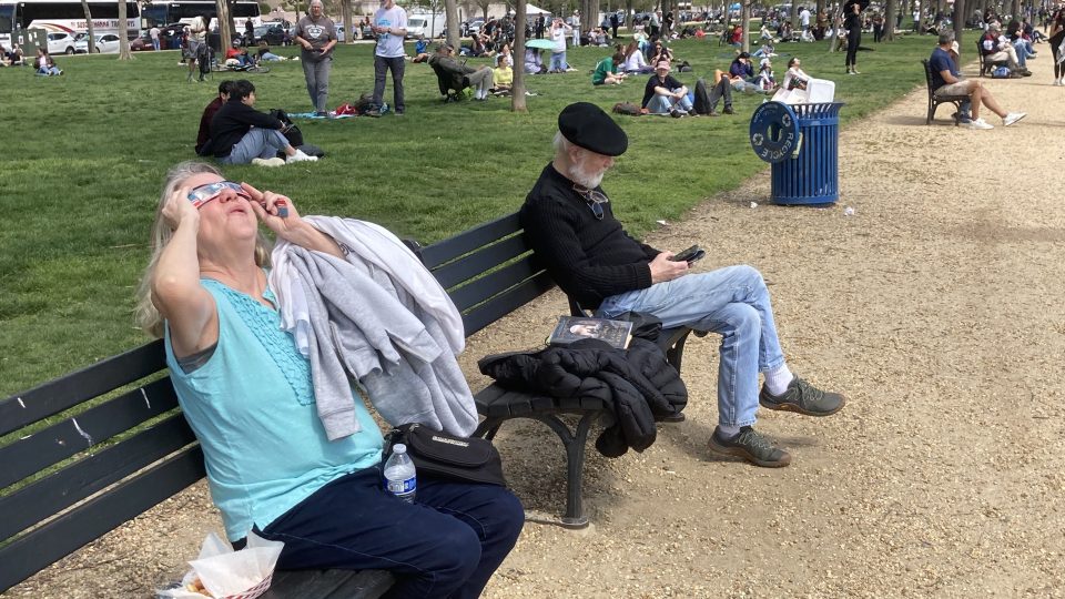 Obyvatelé Washingtonu pozorují částečné zatmění slunce v parku National Mall