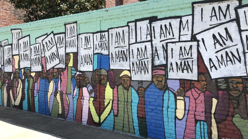 Streetartová malba na zdi v Memphisu odkazuje na slavnou fotografii z doby přesně před 50 lety, na níž Afroameričané pochodují během stávky za svoje občanská práva. V rukou drží transparenty s nápisem „Jsem člověk“..